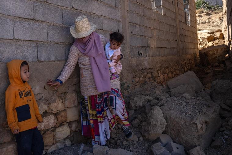 A woman carries a baby over the rubble of a collapsed building on Sept. 13 in Ardouz, Morocco, with her other child close by.