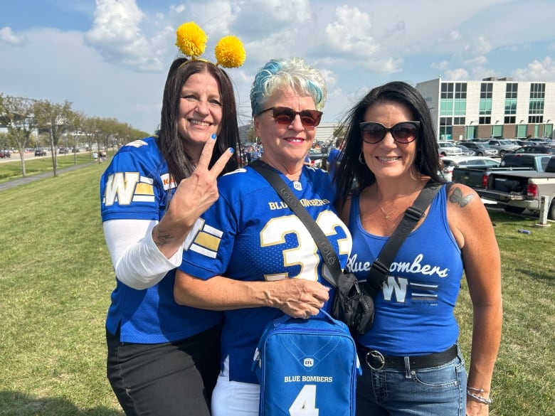 Three women wearing blue jerseys stand on a lawn.