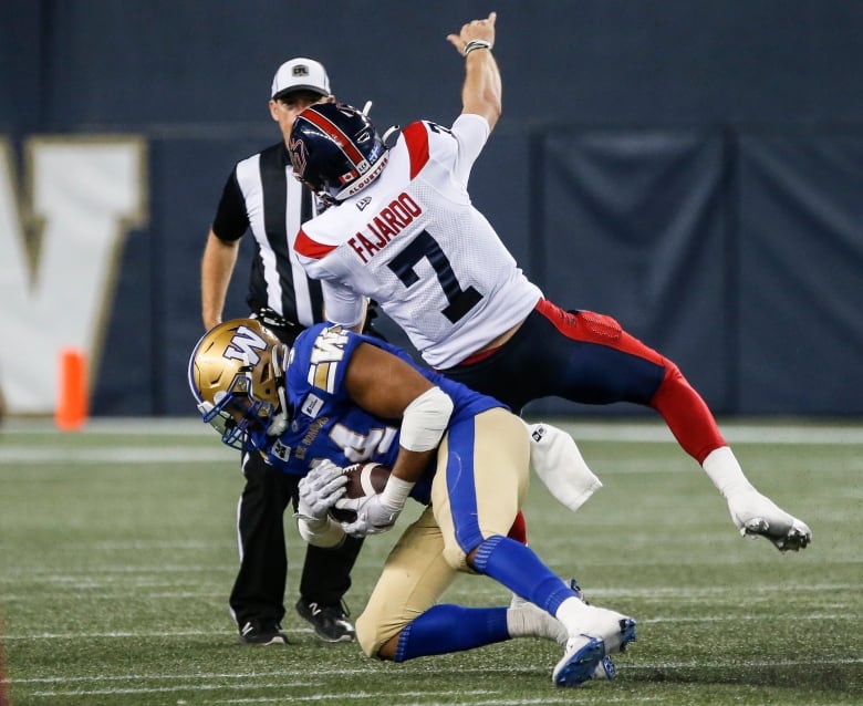 A football player in blue and gold holds a football while another player in white and red falls.