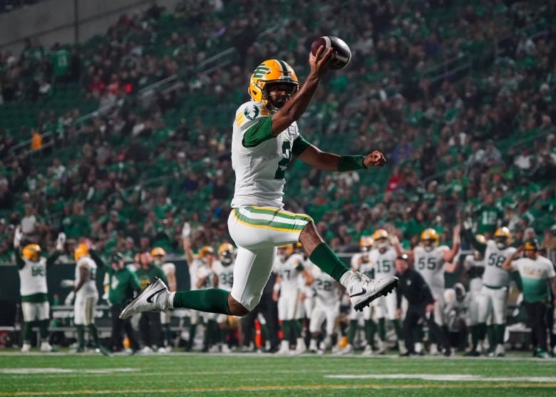 A player in a white jersey leaps into the air with his outstretched hand holding a football