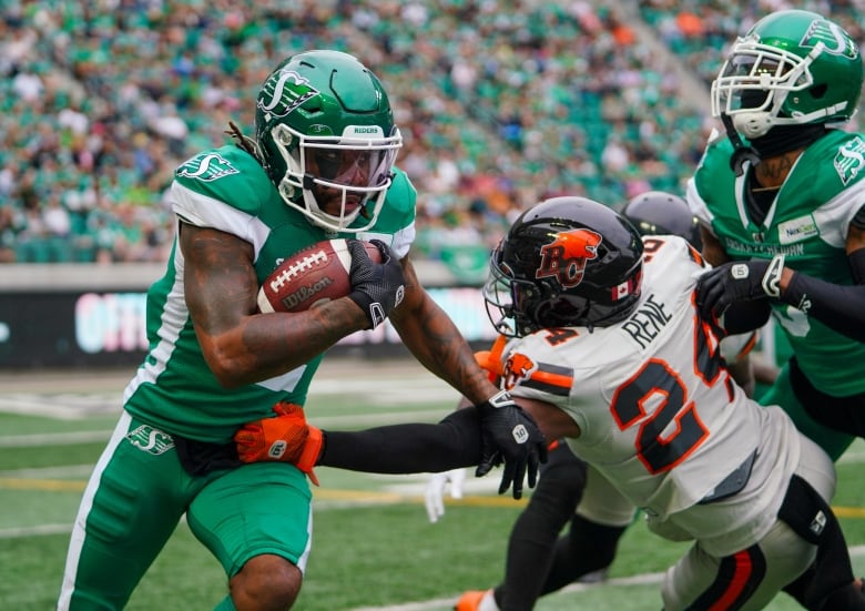 Roughrider punt returner Mario Alford is running with the ball and a B.C. Lion's player is grabbing on to him by the waist