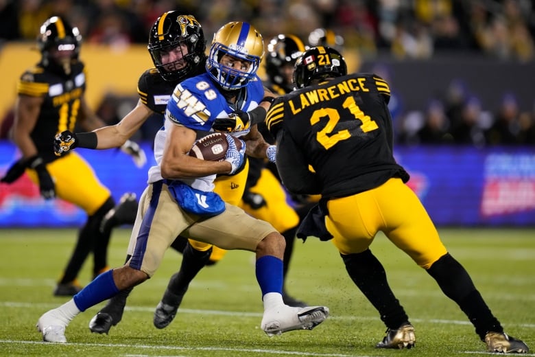 Winnipeg Blue Bombers wide receiver Kenny Lawler (89) runs the ball after a catch as Hamilton Tiger-Cats defensive back Stavros Katsantonis (30) and linebacker Simoni Lawrence (21) defend during first half football action in the 108th CFL Grey Cup in Hamilton, Ont., on Sunday, December 12, 2021.