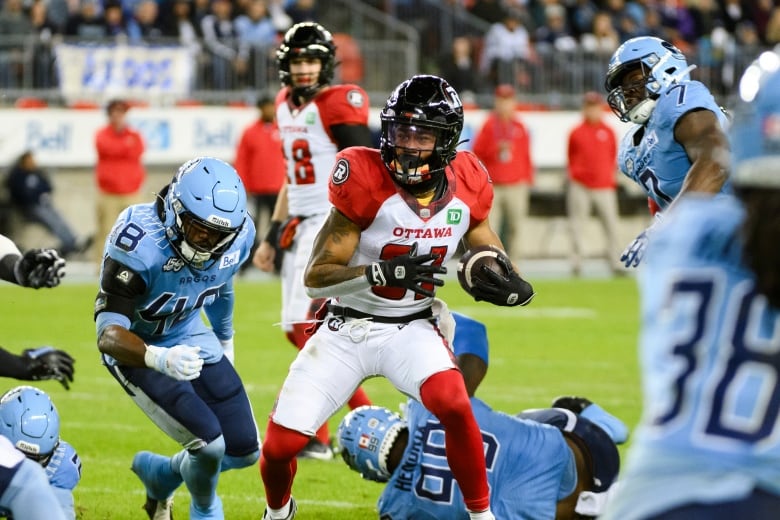 A football player runs with a football while surrounded by several other players.