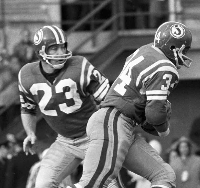 A male football running back takes a hand off from a quarterback.