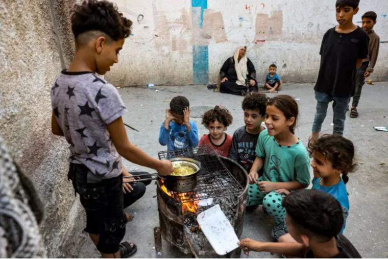 Children sit together around a boy cooking instant noodles on a fire in a makeshift oven from a recycled barrel in Rafah in the southern Gaza Strip on Oct. 31.