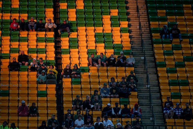 Fans are seen setting in the green and yellow stands of a stadium as they watch a game.