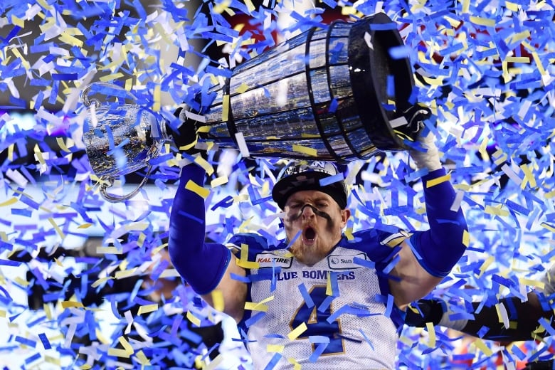 A football player holds up a trophy surrounded by confetti.