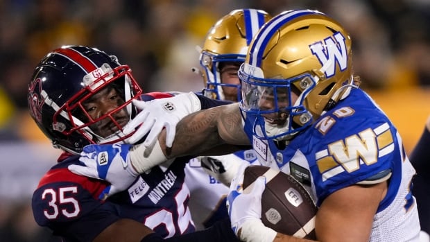 A football player carrying a ball stiff arms a defender.