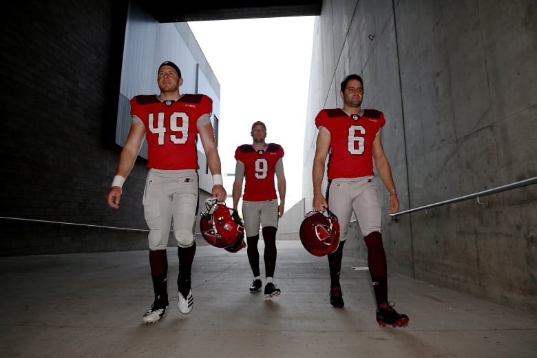 Three football players walk through tunnel from field.