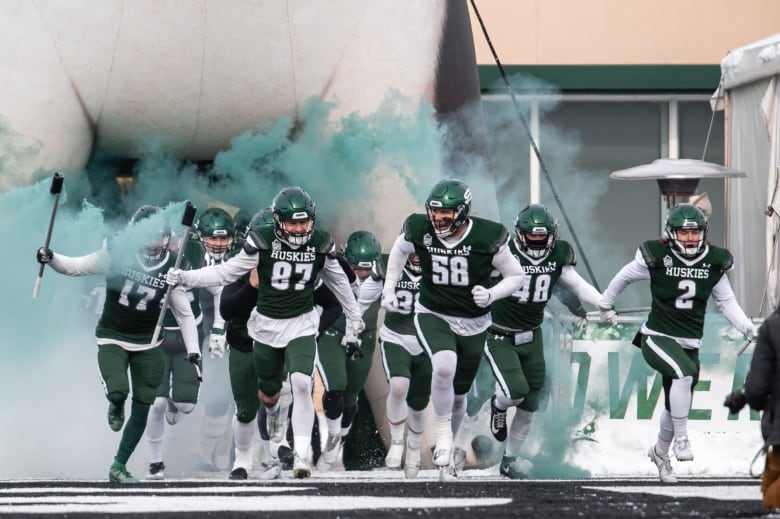 University of Saskatchewan Huskies running out of a tunnel with smoke coming out in the background.