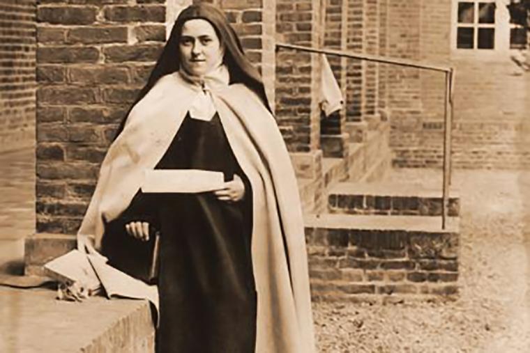 St. Thérèse_of_Lisieux displays a parchment with the words of St. Teresa of Ávila, “I would give a thousand lives to save a soul,” in the courtyard of her Carmel of Lisieux, France, in 1896.