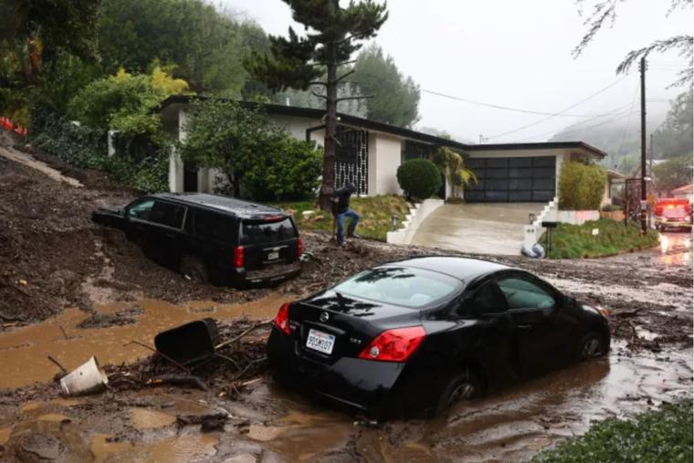 A person attempts to clear away debris from a mudslide as a powerful long-duration atmospheric river storm, the second in less than a week, continues to impact Southern California on Feb. 5, in Beverly Hills, California.