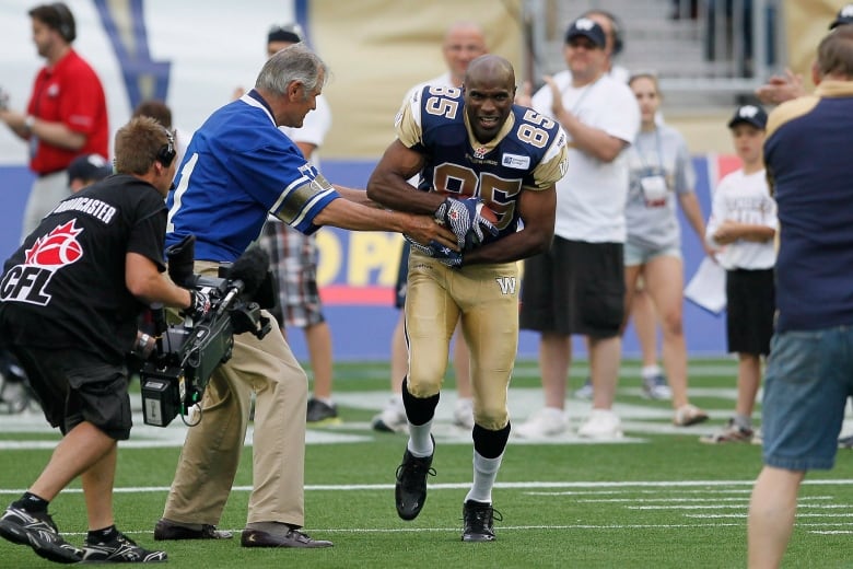 A football player grabs a football from a man to the right of him, during a ceremonial handoff before a game.