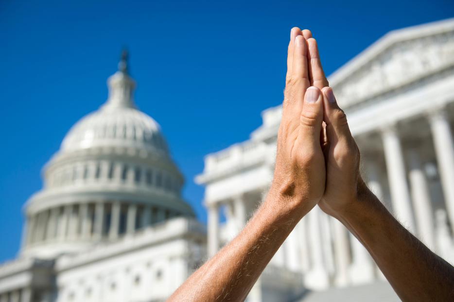 Hands held together in prayer in front of the Capitol building and Supreme Court in Washington, D.C.
