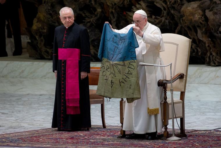 Pope Francis holds a flag of Ukraine that comes from the city of Bucha, just two months into the war with Russia, during the weekly general audience on April 6, 2022 at Pope Paul VI Hall in the Vatican.
