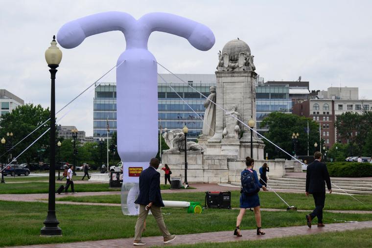 People walk past a 20-foot (6-meter) tall inflatable intrauterine device (IUD) outside of Union Station in Washington, DC, on June 5, 2024.