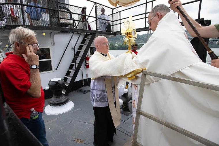 Upon arrival, Bishop Lohse hands Jesus Christ in the Blessed Sacrament to Fr. Roger Landry aboard the vessel ‘Sewickley.’