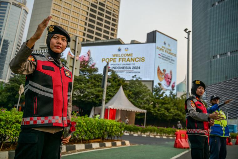 Indonesian police direct traffic next to billboards displaying a welcome message for Pope Francis in Jakarta on September 2, 2024. Pope Francis embarks September 2 on a 12-day trip to Southeast Asia including Indonesia, Papua New Guinea, East Timor and Singapore, the longest and farthest of his papacy.