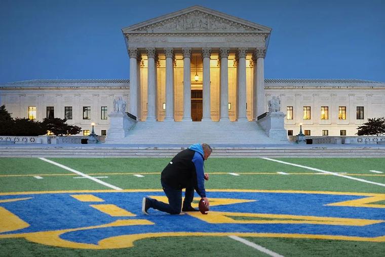 Coach Joe Kennedy kneels on the football field.