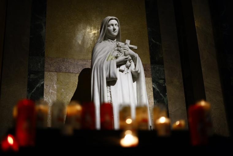 Candles lit by worshippers burn under a statue of St. Thérèse at the Basilica of St. Thérèse of Lisieux in Lisieux, France.