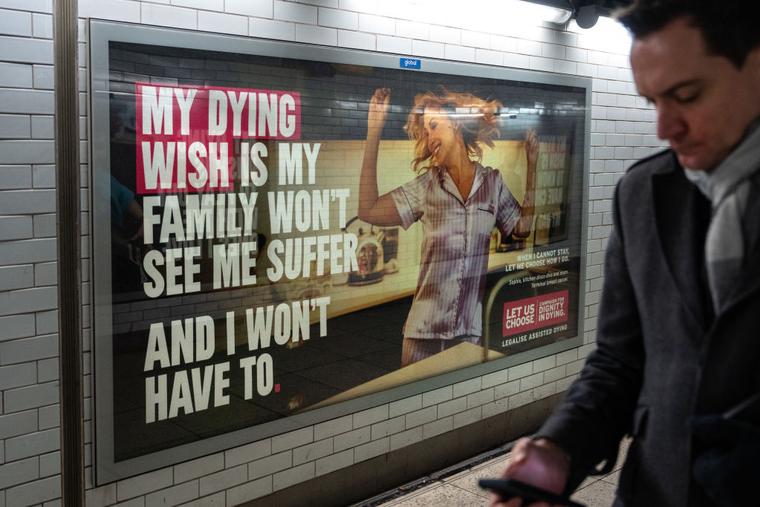 A man walks past a poster advocating legally assisted suicide by the campaign group Dignity in Dying in Westminster underground station on November 28, 2024 in London, England.
