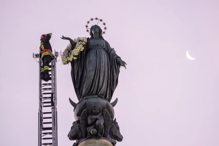 A firefighter in Rome pays tribute to the Blessed Virgin Mary by laying a wreath of fresh flowers at her statue atop a column near the Spanish Steps at dawn on Dec. 8, 2023.