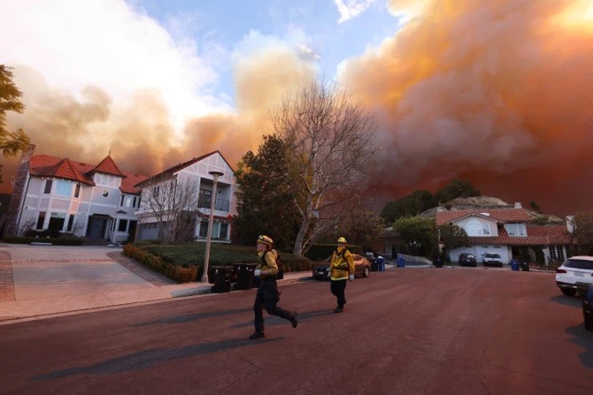 Firefighters run as a brush fire burns in Pacific Palisades, California, on Jan. 7, 2025. A fast-moving brushfire in a Los Angeles suburb burned buildings and sparked evacuations as “life-threatening” winds whipped the region.