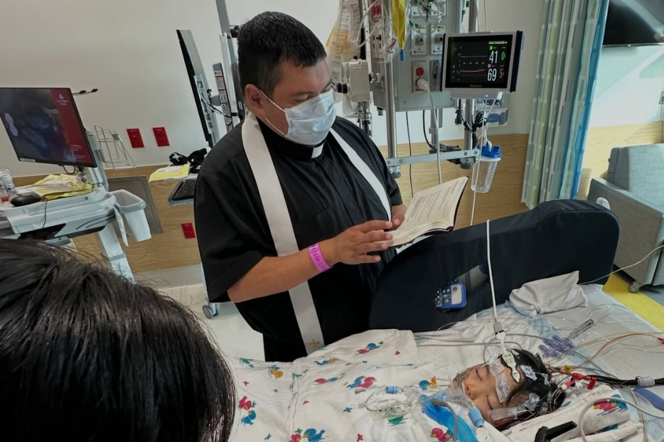A priest prays for young Micah in the hospital.