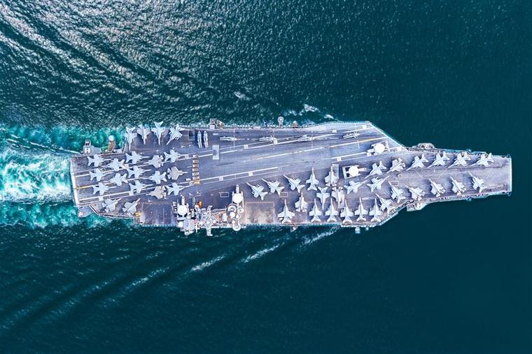 A U.S. Navy Nimitz-class aircraft carrier sails at sea with fighter jets and helicopters parked on its flight deck.