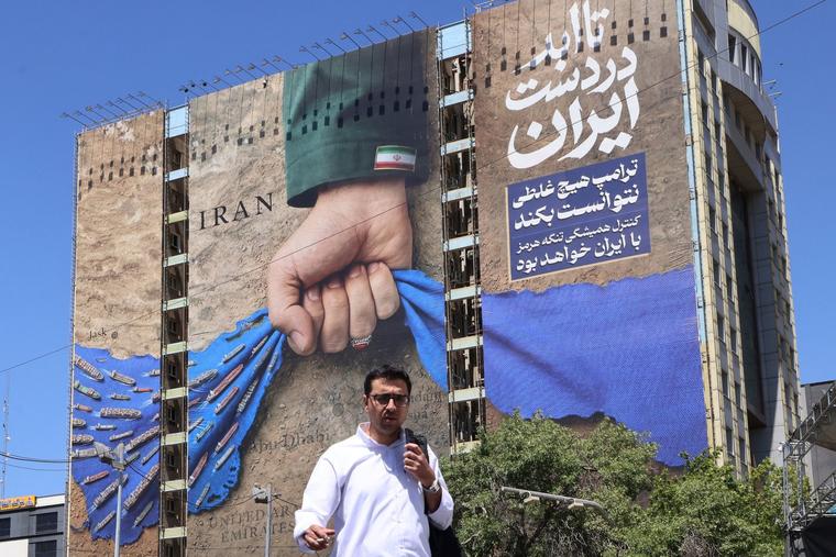A man crosses a street past a billboard on the facade of a building depicting the Strait of Hormuz with a caption in Persian reading "Forever in Iran's Hand" in Tehran’s Vanak Square on May 25.
