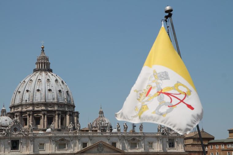 The flag of Vatican City with St. Peter’s Basilica in the background.